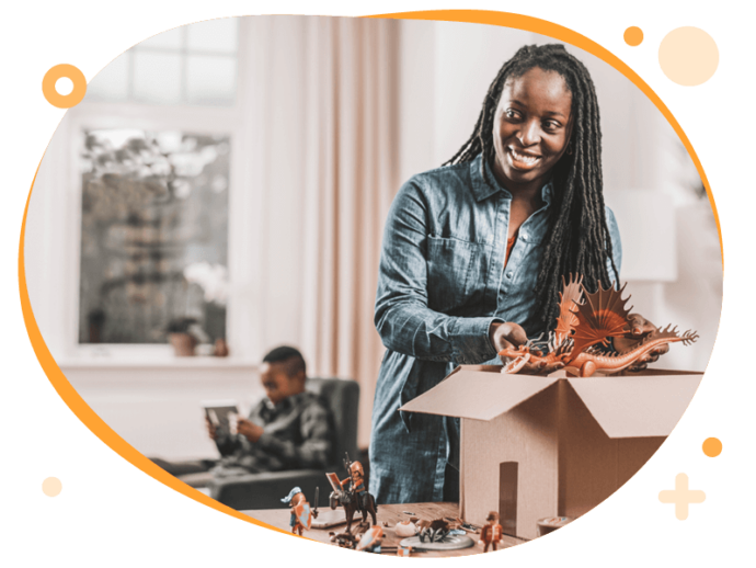 Vrouw is een pakket aan het inpakken met speelgoed. Op de achtergrond is haar zoontje op een ipad aan het kijken.