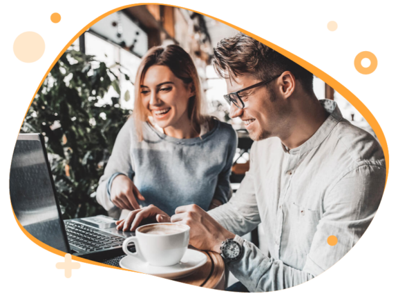 Man en een vrouw zitten achter een laptop en lachen naar het scherm. Naast de laptop staat een kop koffie.