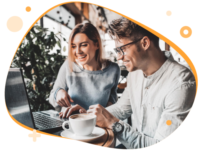 Man en een vrouw zitten achter een laptop en lachen naar het scherm. Naast de laptop staat een kop koffie.